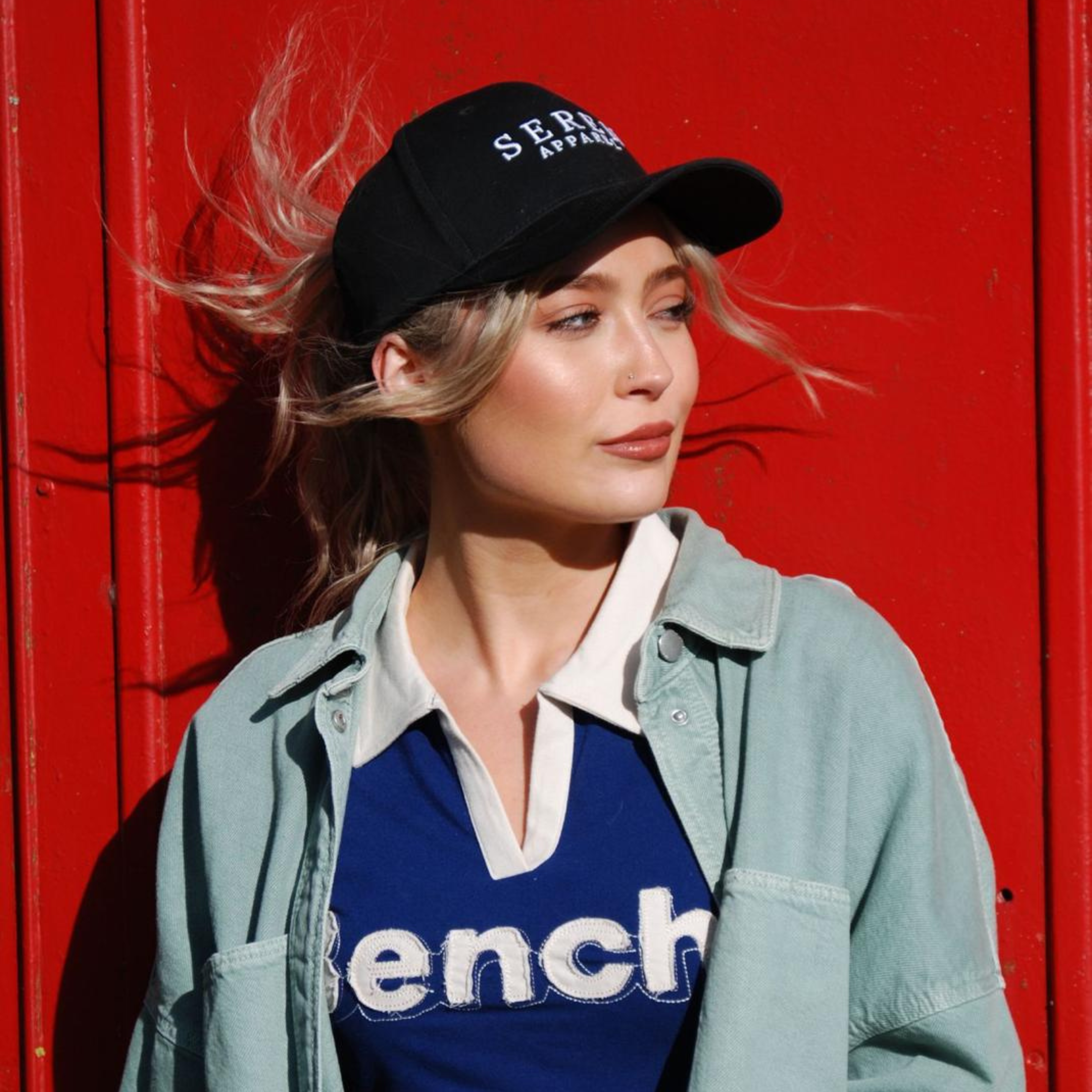 Woman wearing a black ponytail baseball cap and blue shirt against a red background