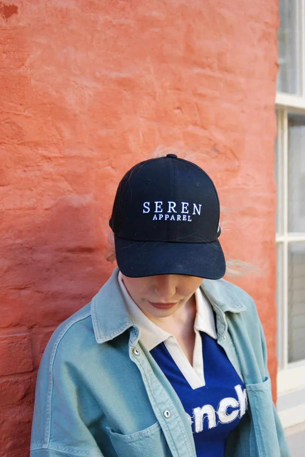 Person wearing a black ponytail baseball cap with 'Seren Apparel' text against a red brick wall.