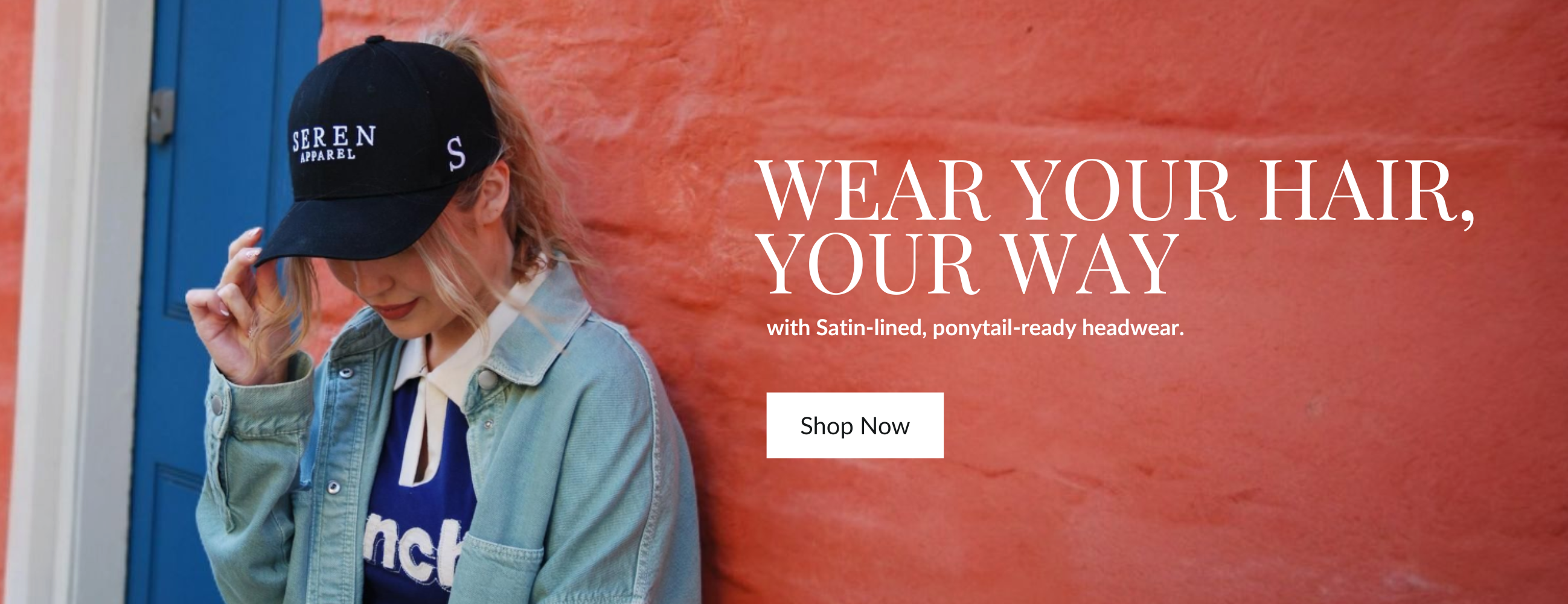 Person wearing a ponytail baseball cap with text on it, standing against a red wall with promotional text.