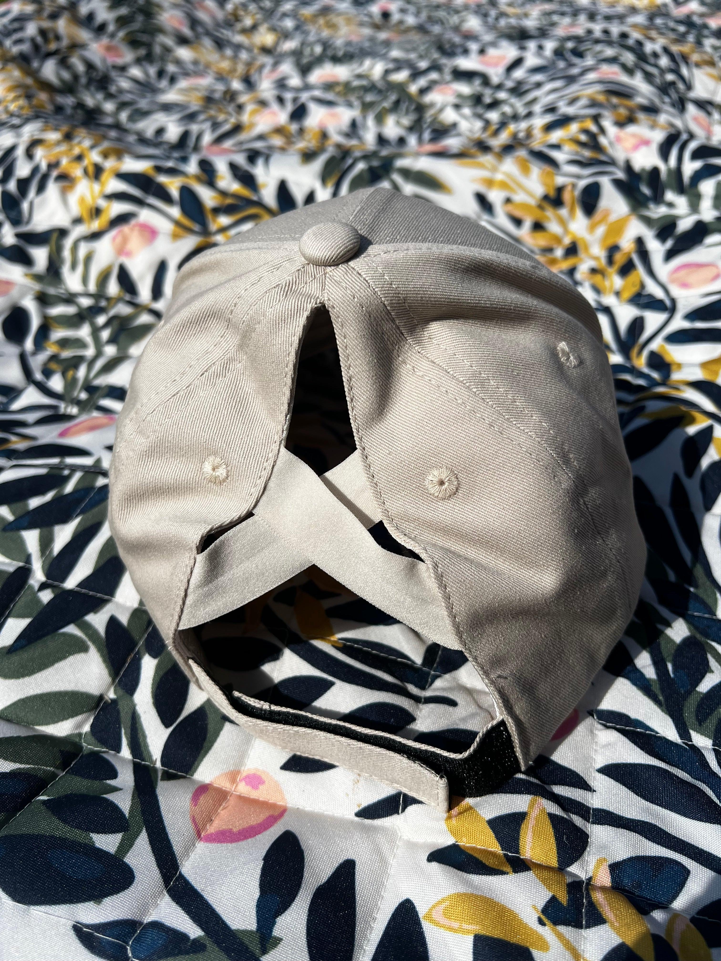 Beige ponytail baseball cap on a floral-patterned fabric background