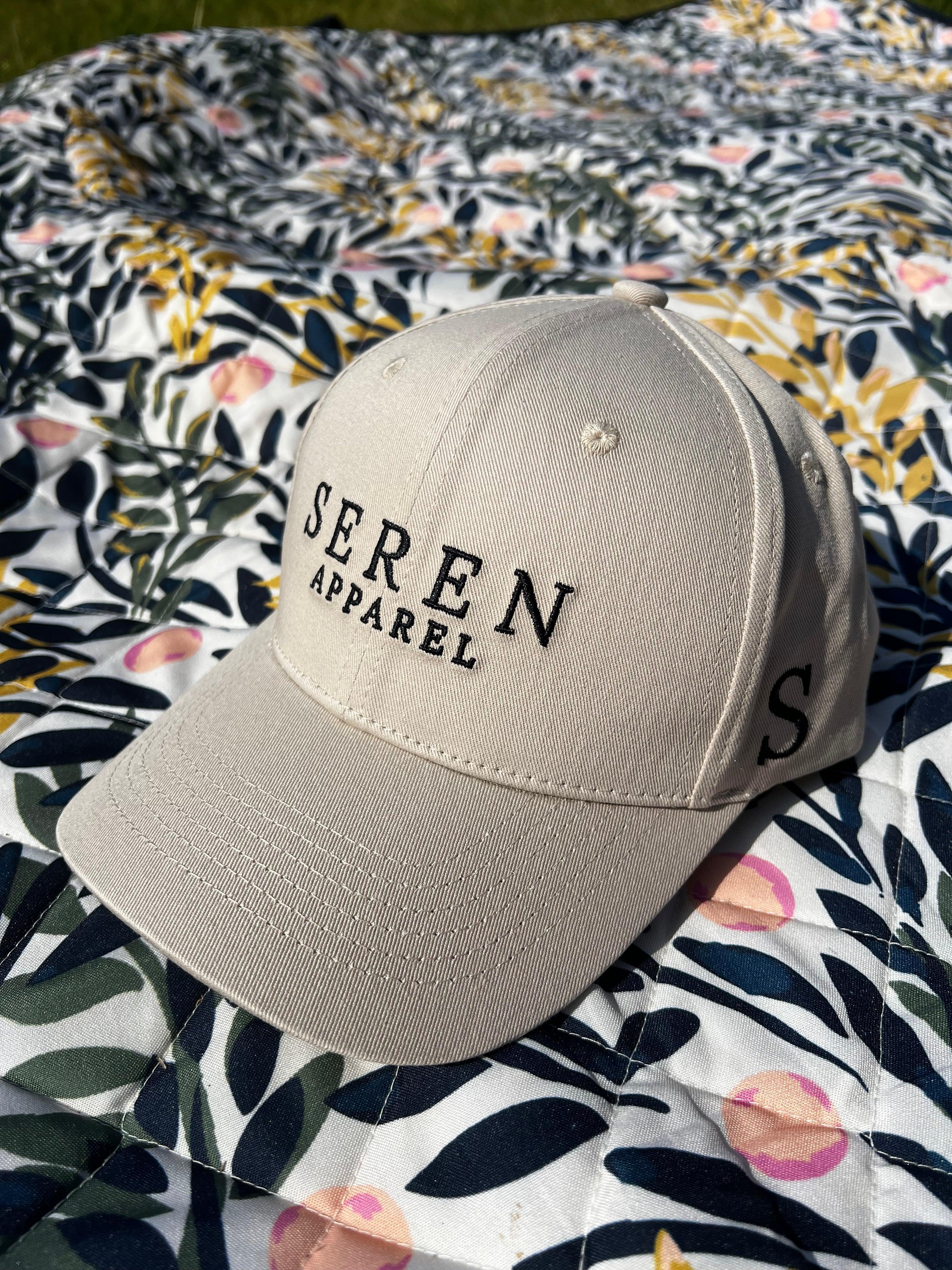 Beige ponytail baseball cap with 'Seren Apparel' branding on a floral fabric background