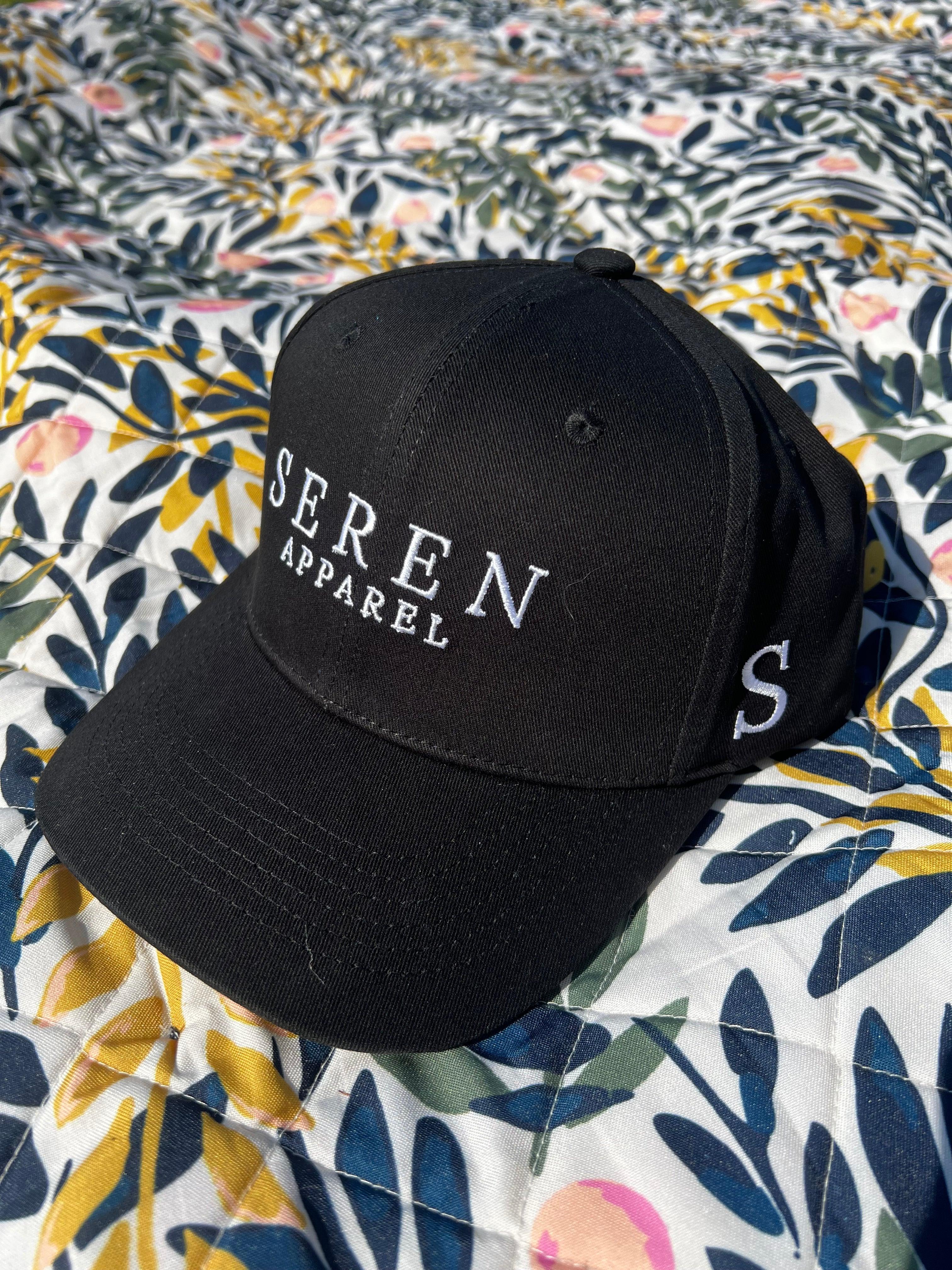 Black ponytail baseball cap with 'Seren Apparel' logo on a floral fabric background