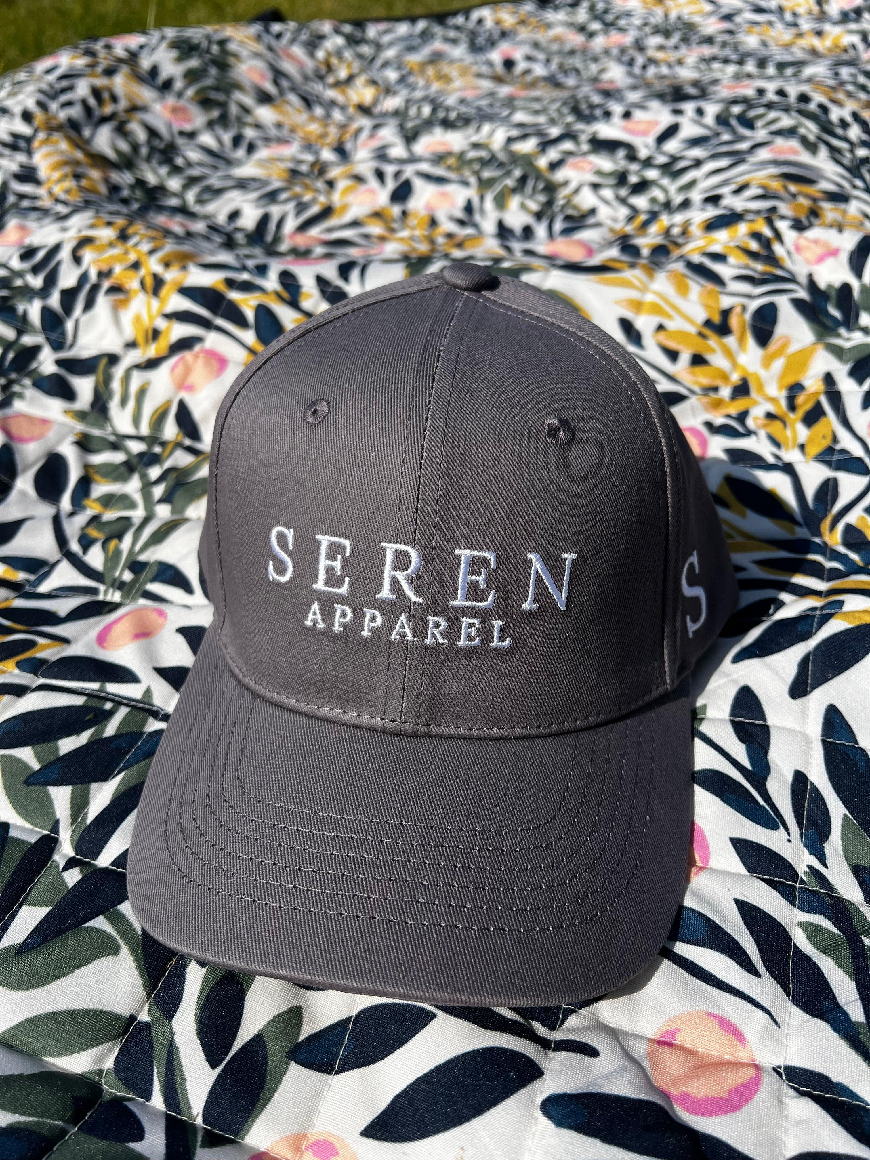 Grey ponytail baseball cap with 'Seren Apparel' logo on a floral fabric background