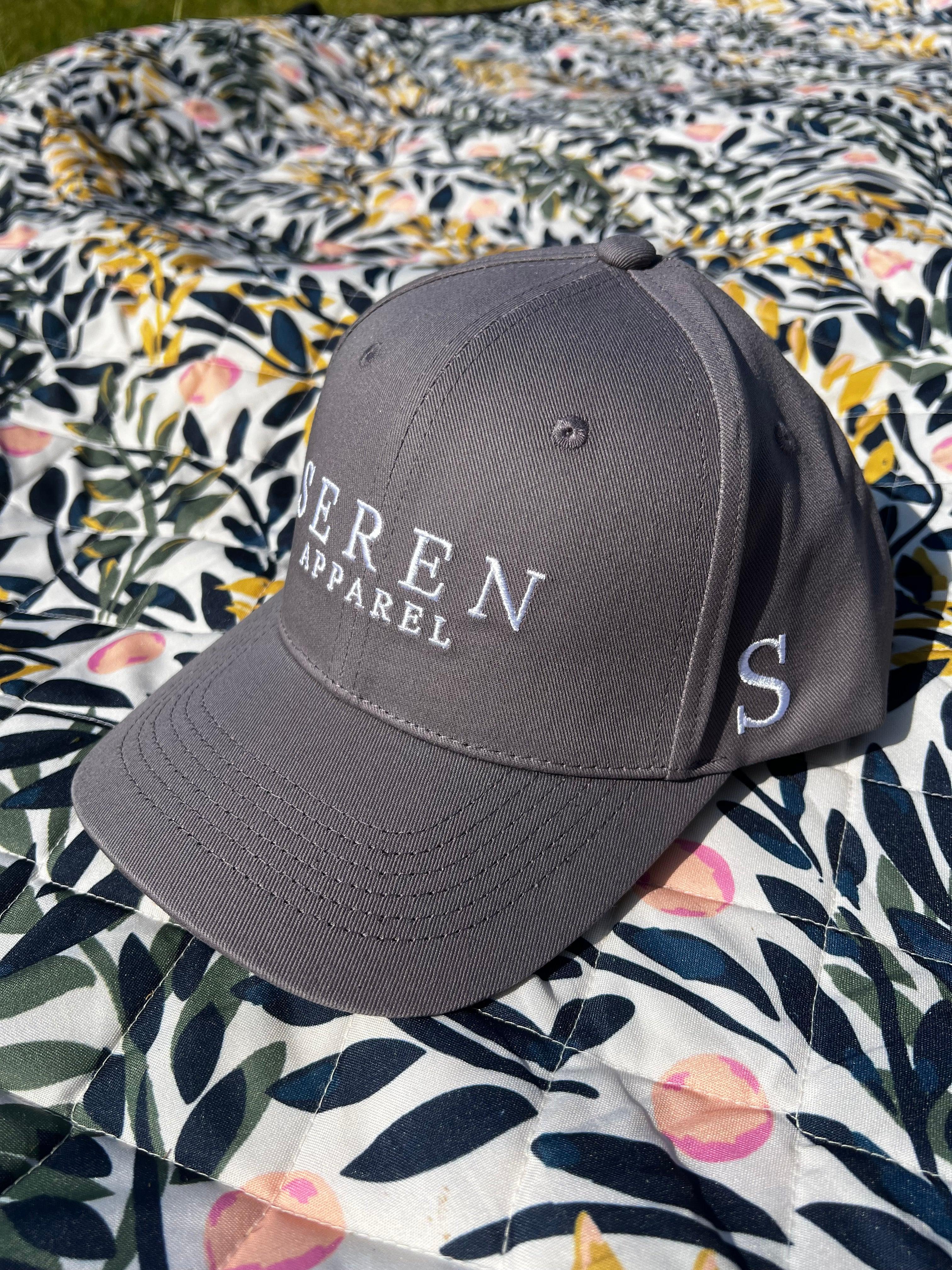 Grey ponytail baseball cap with 'Seren Apparel' logo on a floral blanket