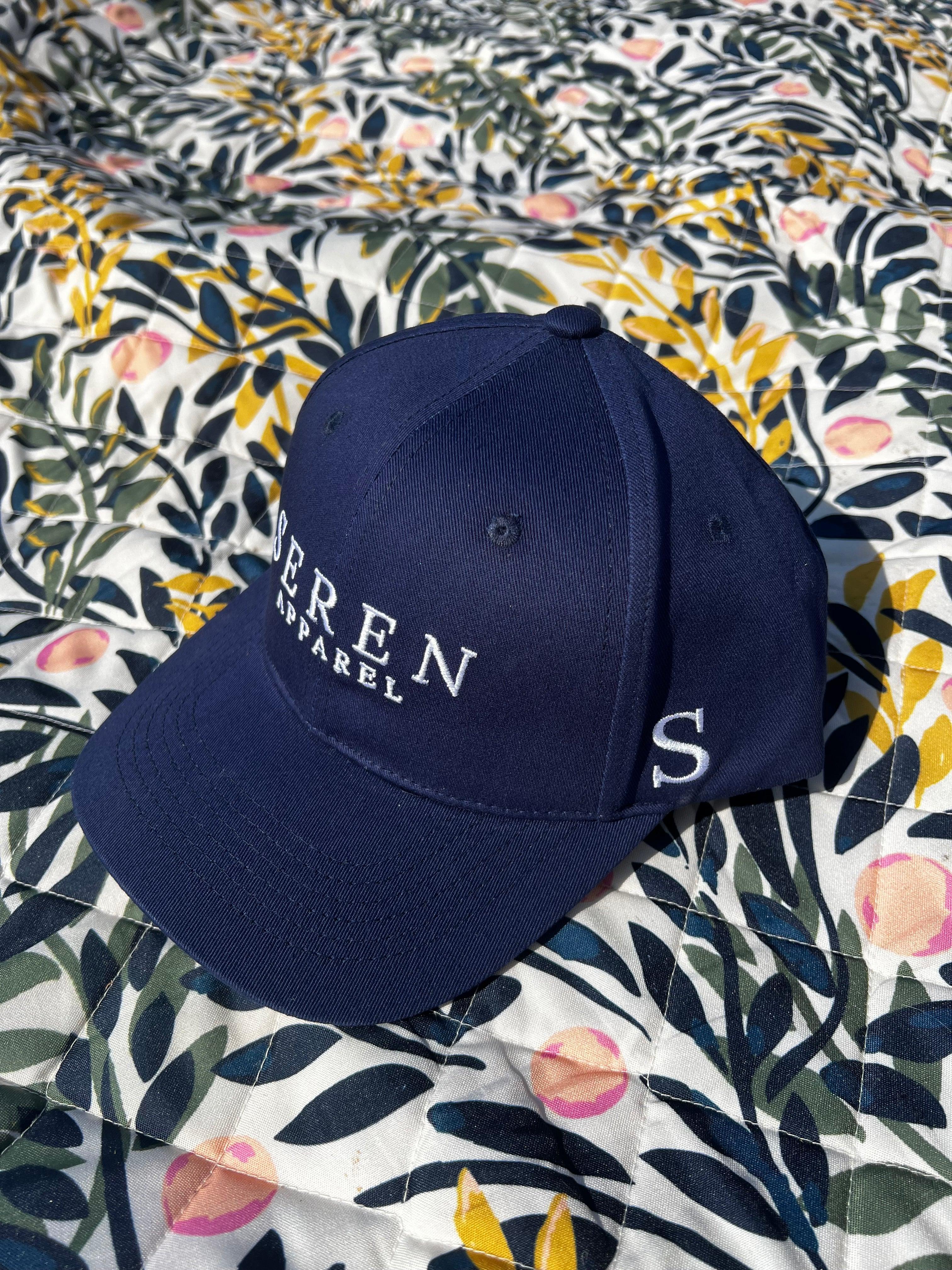 Navy blue ponytail baseball cap with 'Seren' branding on a floral fabric background