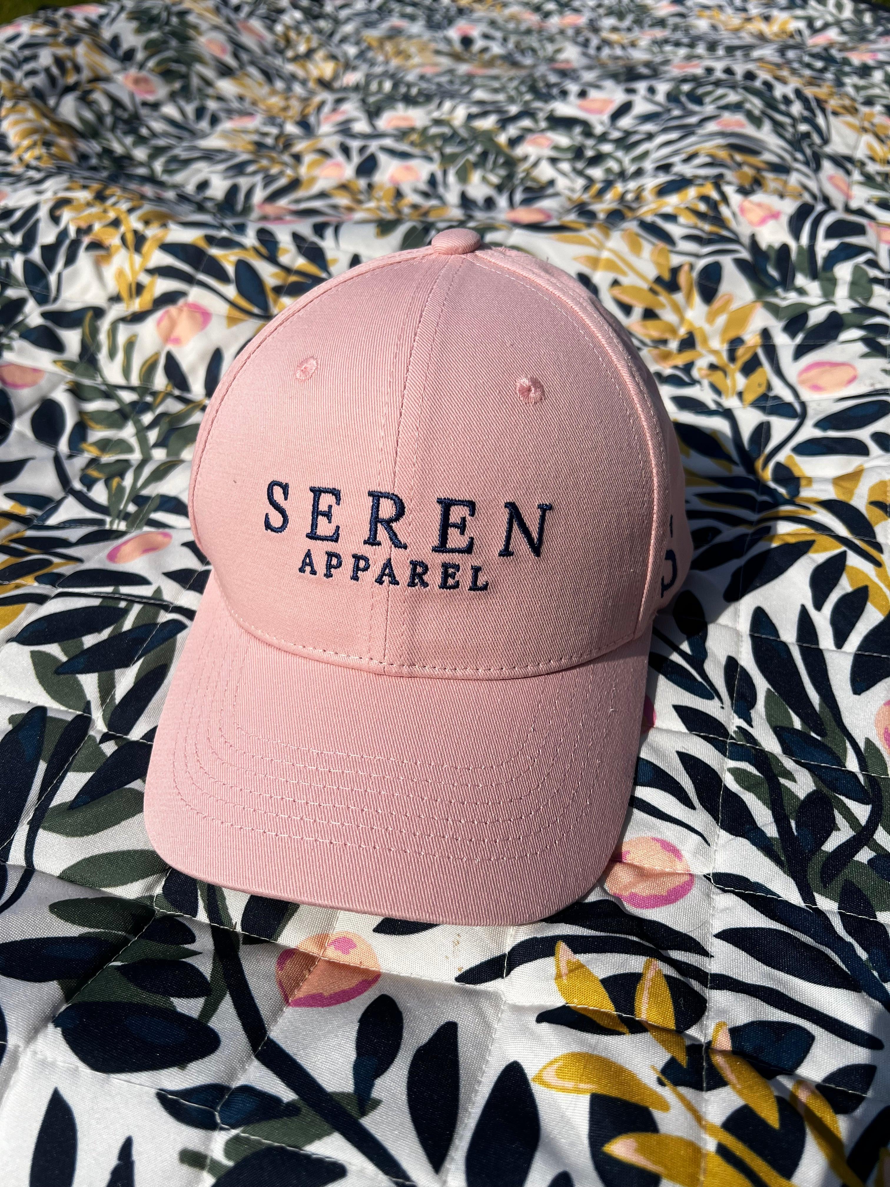 Pink ponytail baseball cap with 'Seren Apparel' text on a floral fabric background
