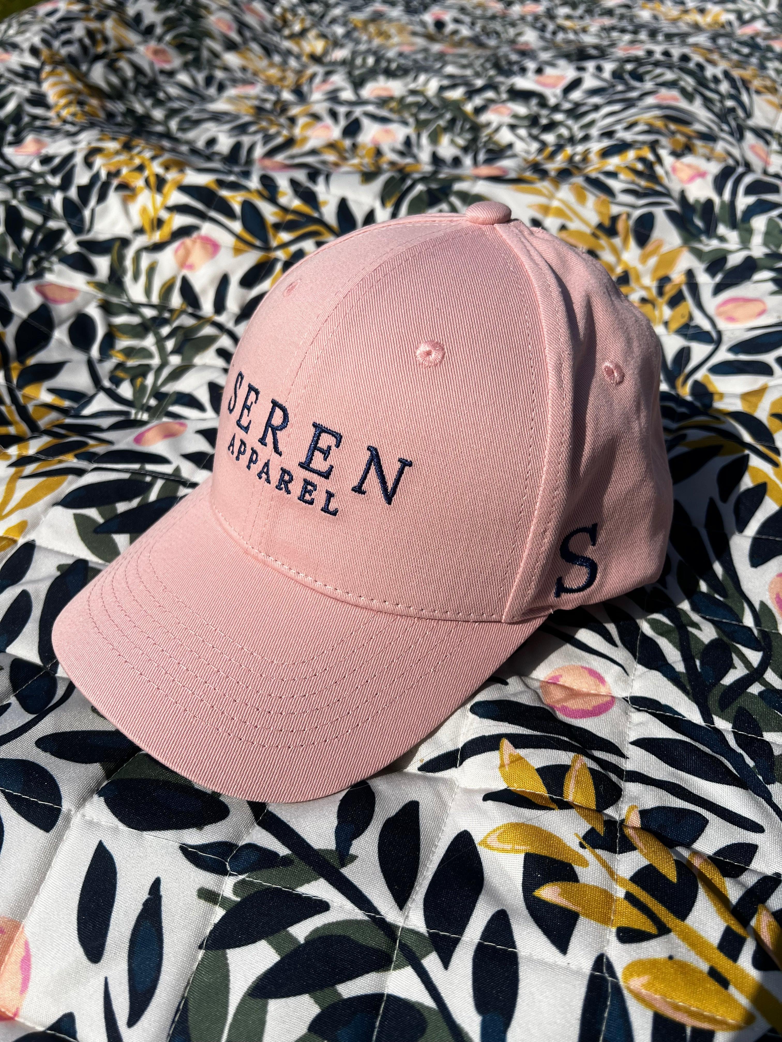 Pink ponytail baseball cap with 'SEREN Apparel' branding on a floral fabric background