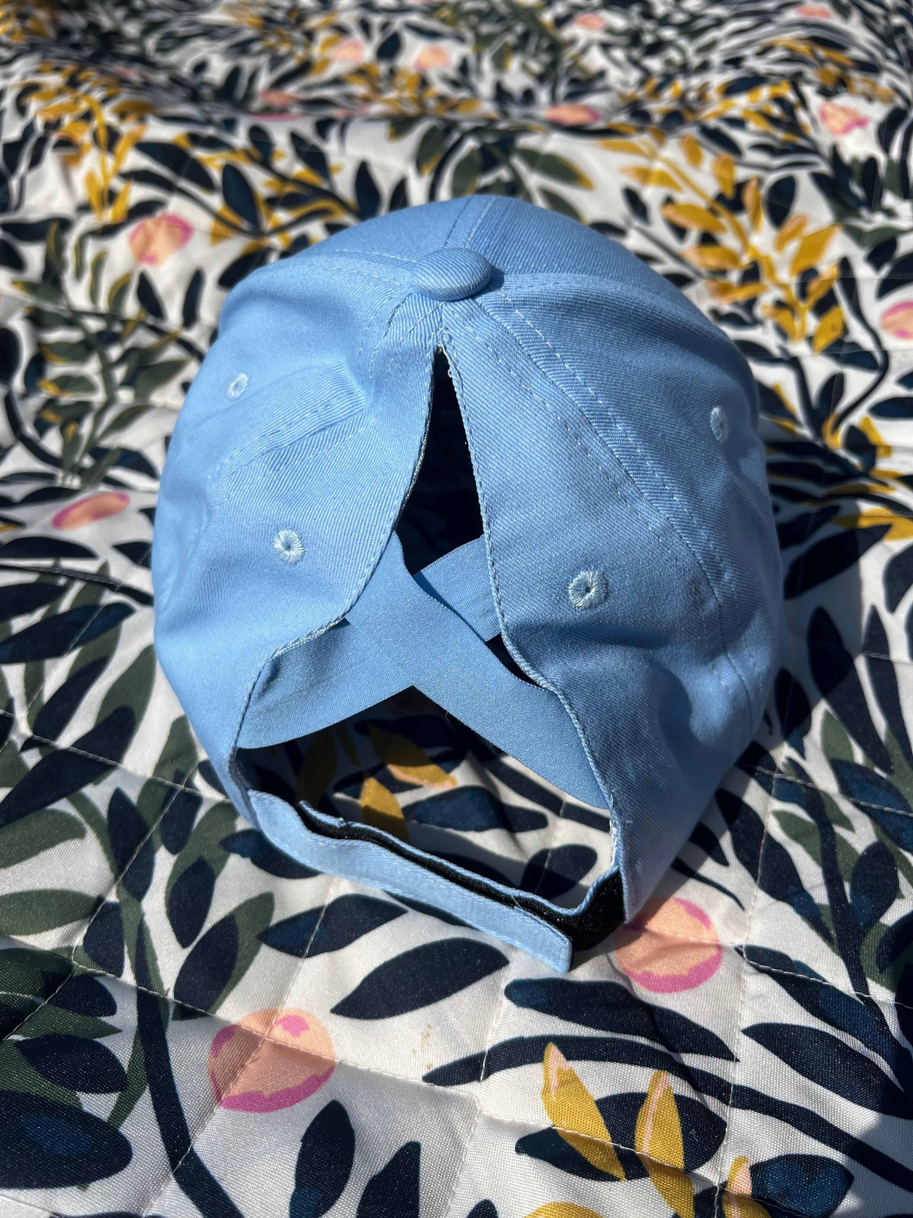 Light blue ponytail baseball cap on a floral-patterned fabric background